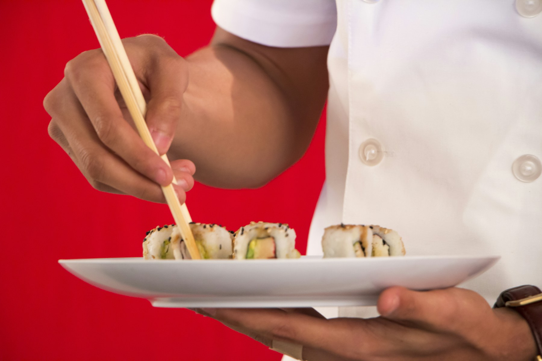 Persona sujetando palillos junto a un plato de sushi